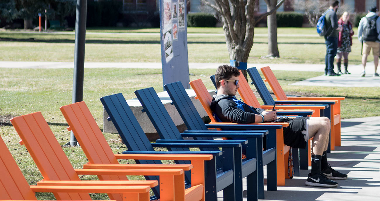 Student sitting outside in a chair, using his phone.