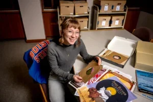 HCS student Cora Lee Oxley thumbing through some vinyl records on a large table with boxes in the background.