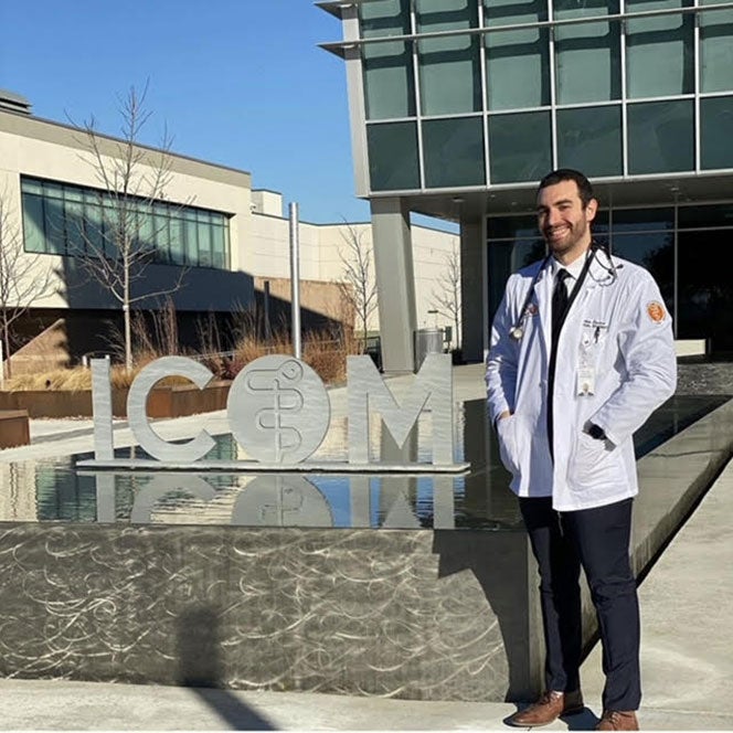Nathan Epstein poses by ICOM statue in a fountain with his white coat and stethoscope