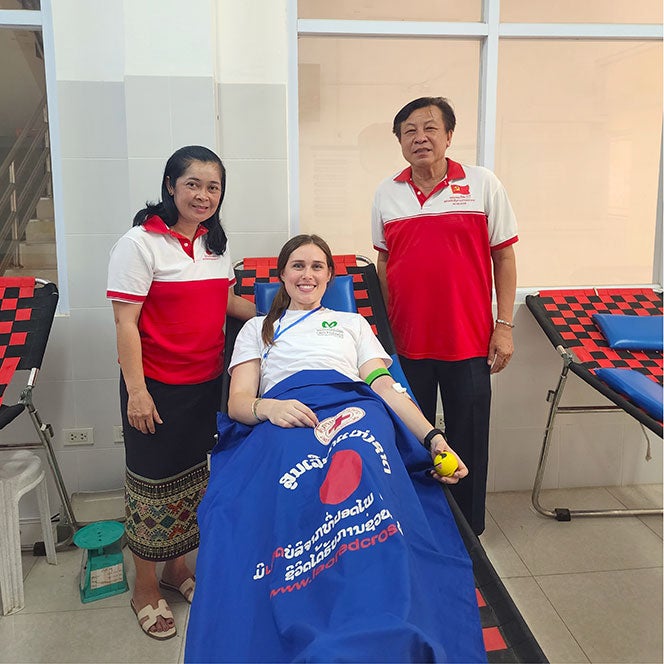 Anastasia Tracy lays on a cot surrounded by two Laotian medical staff 