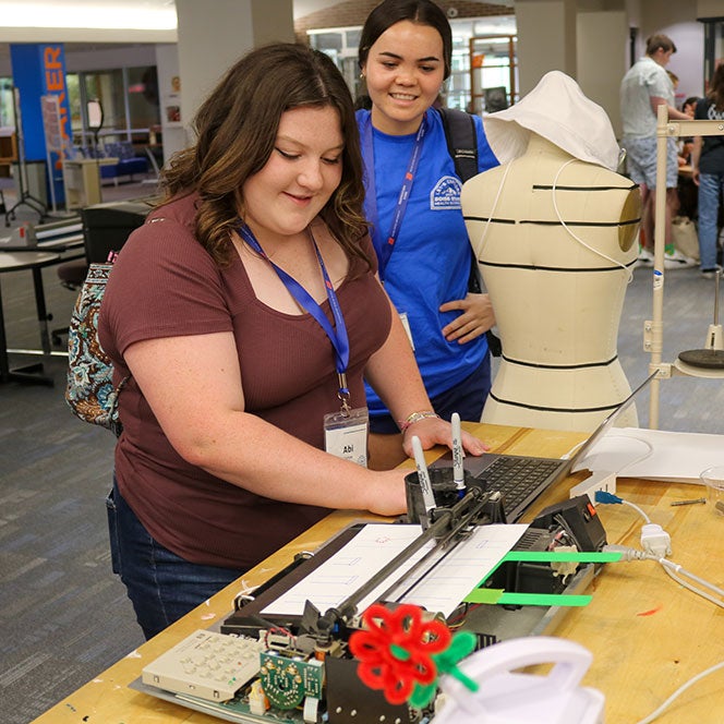 Brooke Brody, camp coordinator, looks on as Abi tries the Axidraw in the Maker Lab