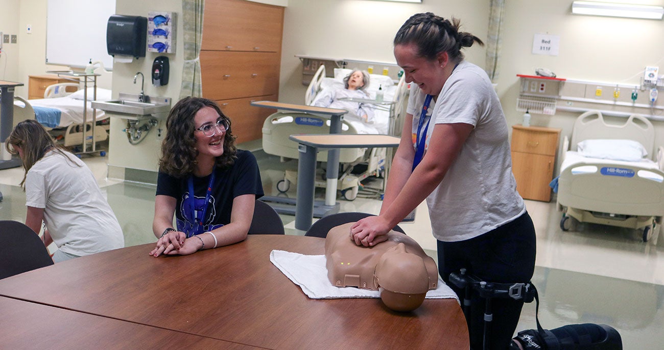 Calista looks on as Sydney practices CPR on a manikin torso during the nursing demonstrations.