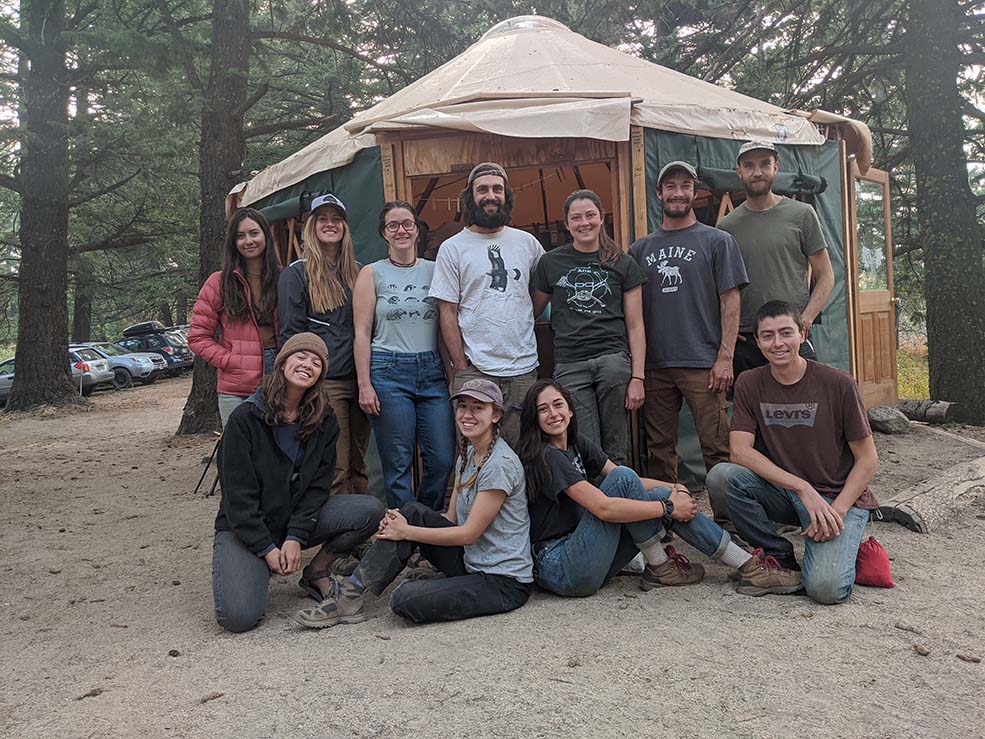 a group of young biologists stand in the forest in front of a yurt