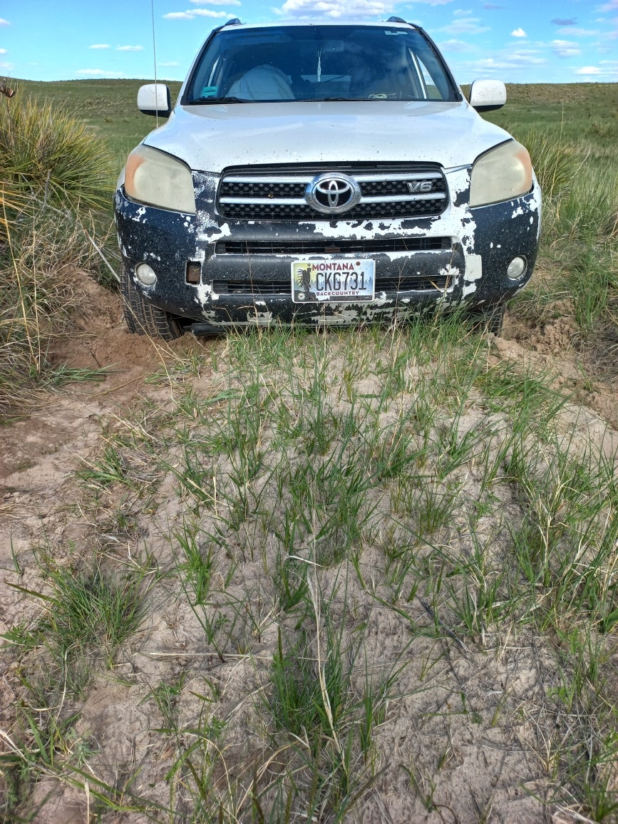 a toyota SUV parked in a very sandy two-track "road". The front bumper of the truck is dragging on the sand and you can see piles of fresh sand around the wheels where they have been spinning, stuck.