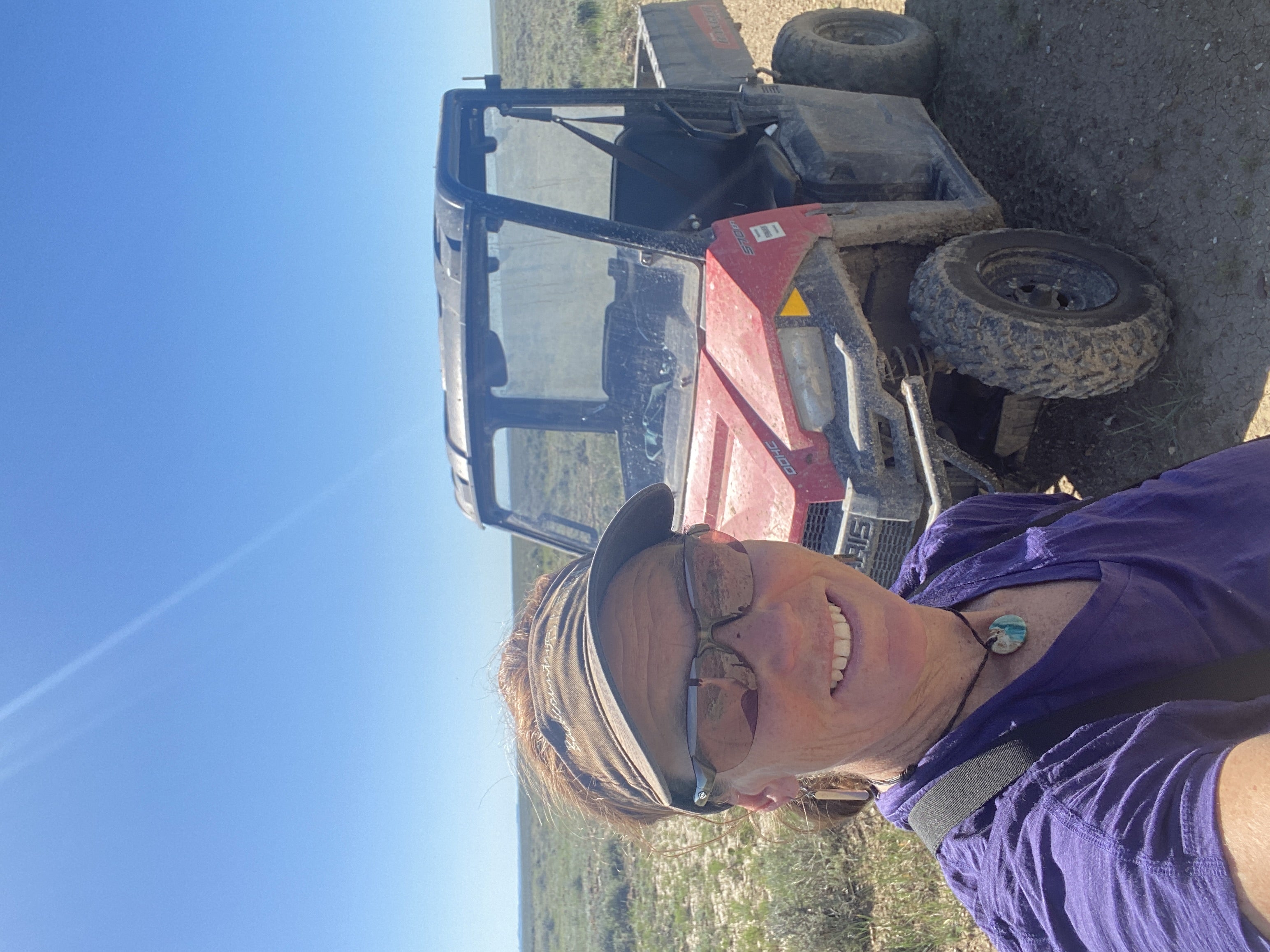 image show a biologist smiling for a selfie with a red UTV vehicle behind her