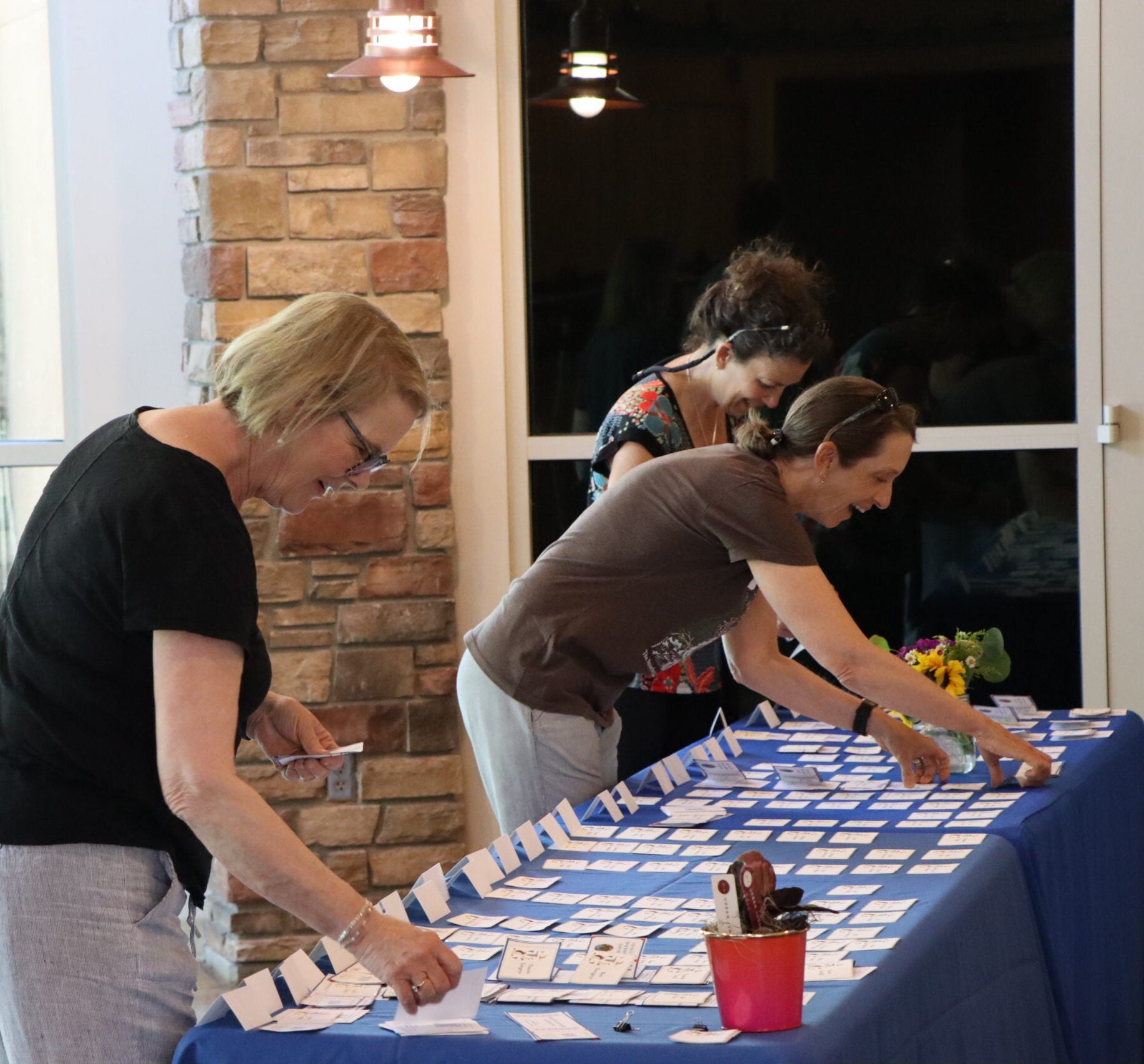 three smiling women work sorting nametags that are laid out on a blue tablecloth