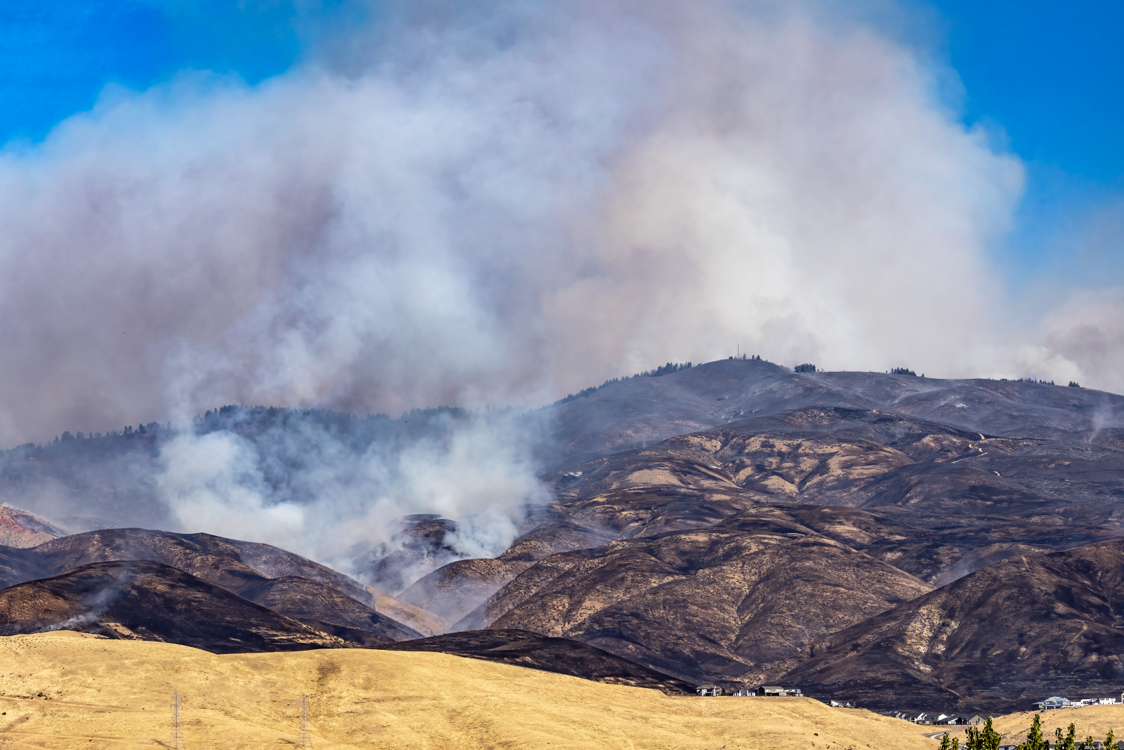 a view from the bottom of the boise foothills showing lucky peak completely blackened by a wildfire. the radio tower is visible on top, obscured by billowing smoke