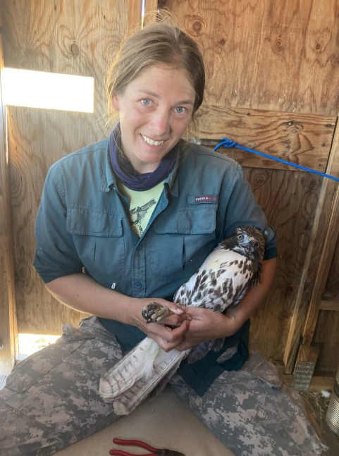 Waas smiles happily at the camera and cradles a large hawk in her arms. her hands are securely holding the hawk's talons.