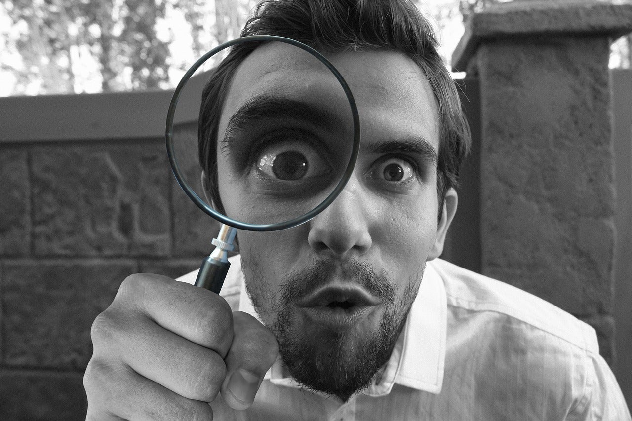Man holding a magnifying glass over one of his eyes and looking intently at the viewer
