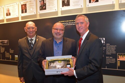 Three men smiling around a plaque.