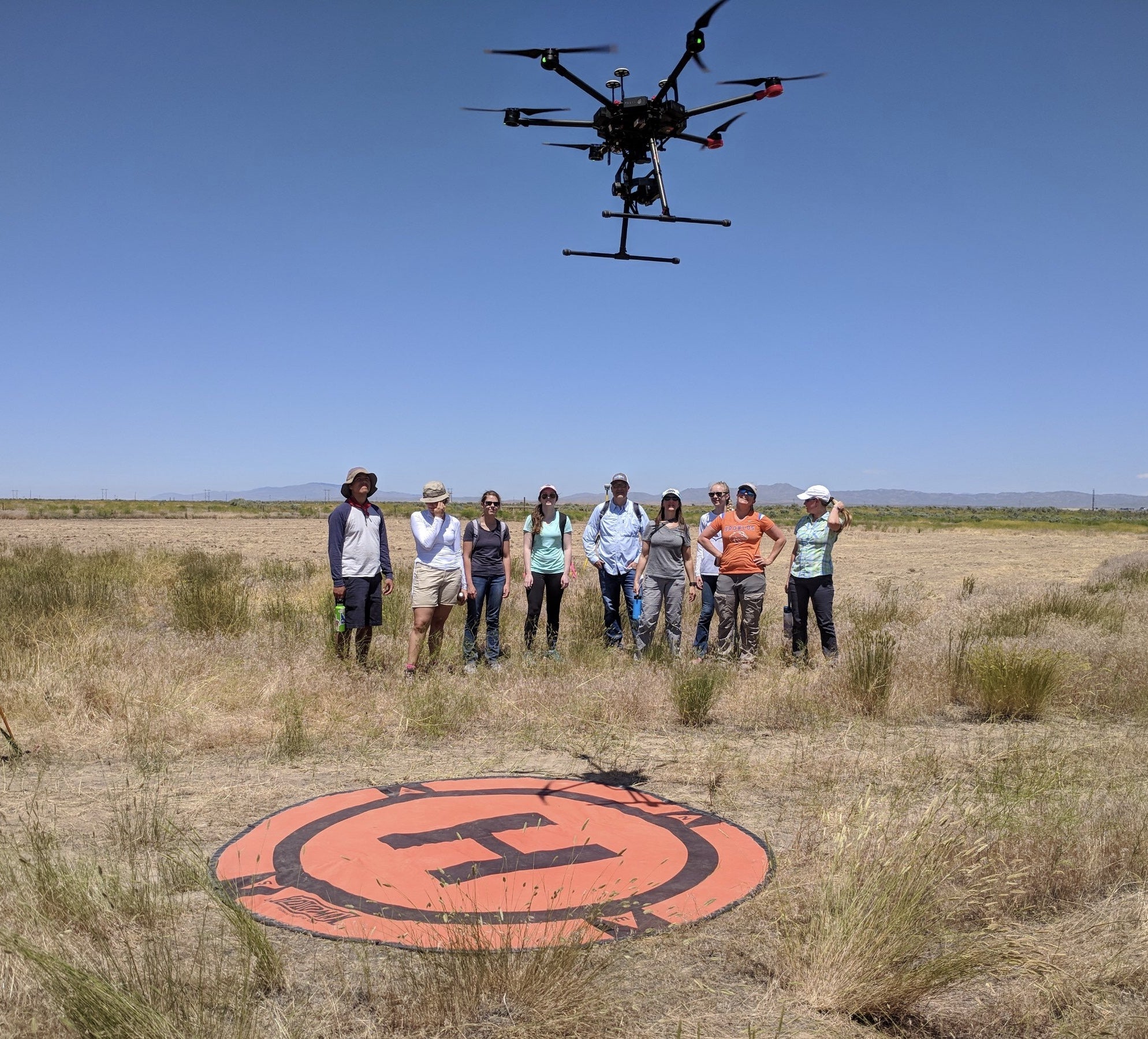Group of people in rangeland watch drone ascend