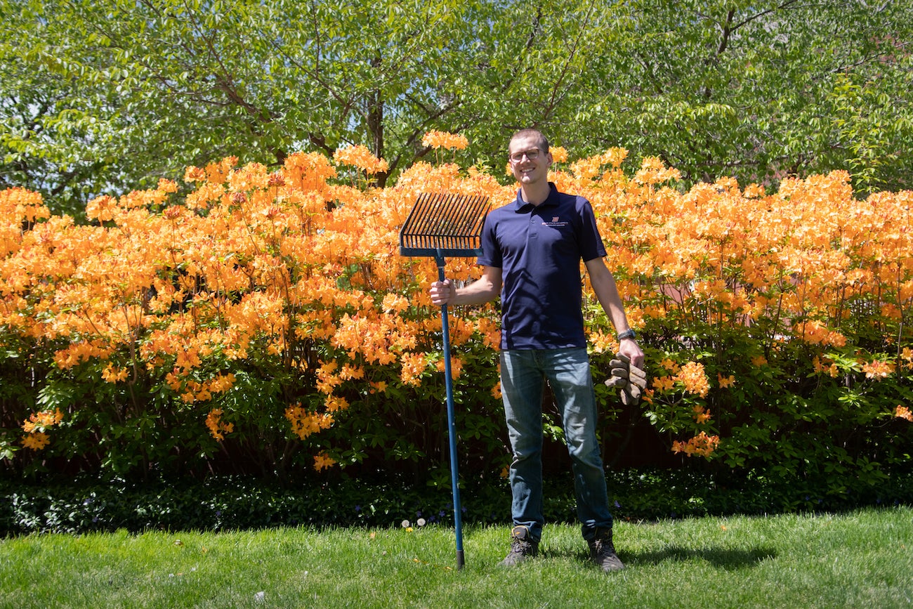 Evan Hershey holding a rake in front of some flowers