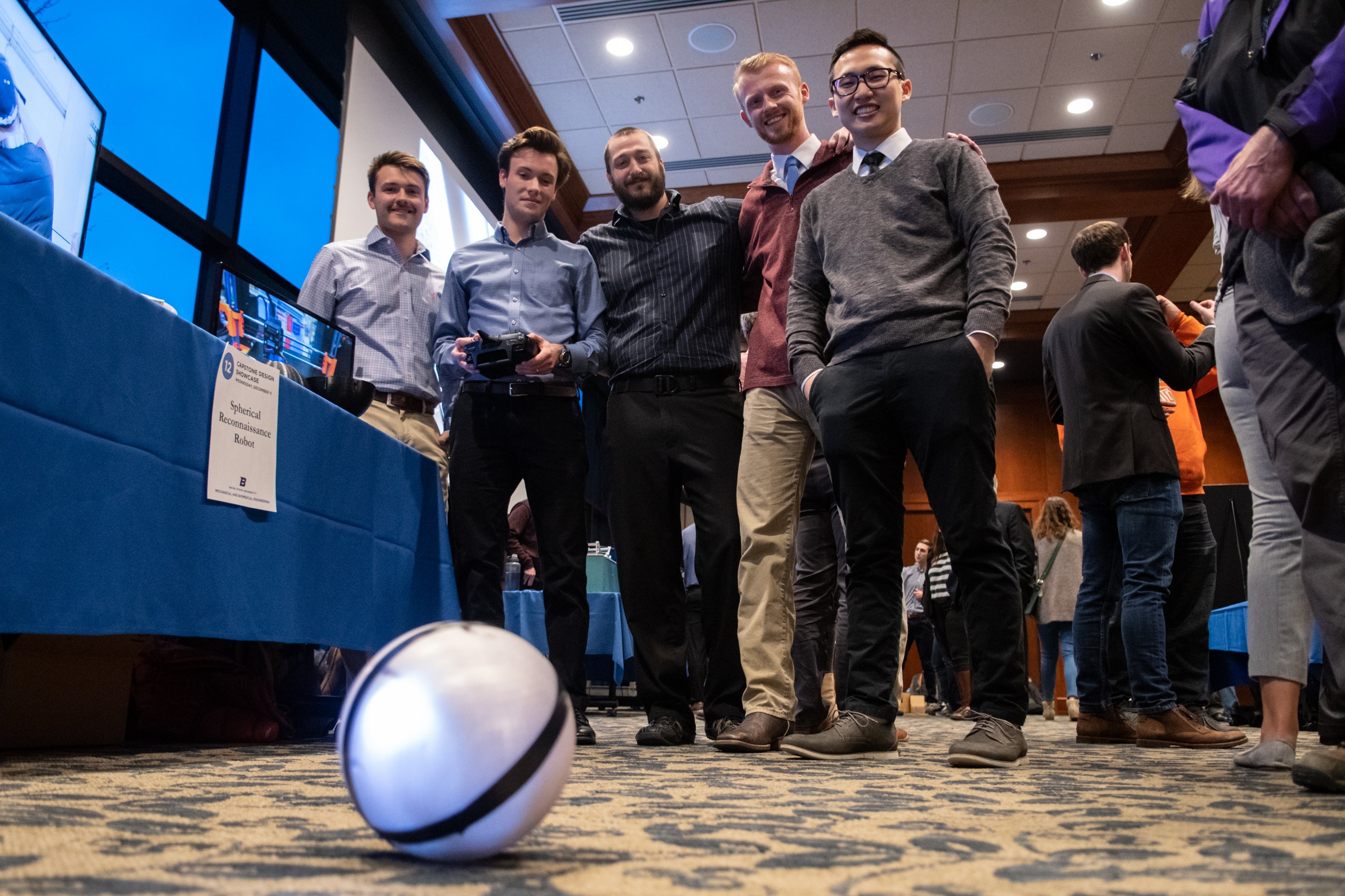 Team of students look down at spherical robot on ground