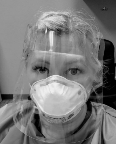 Melanie Kanawyer wears a clear face shield, face mask, and protective overshirt to prevent fluid contamination. 