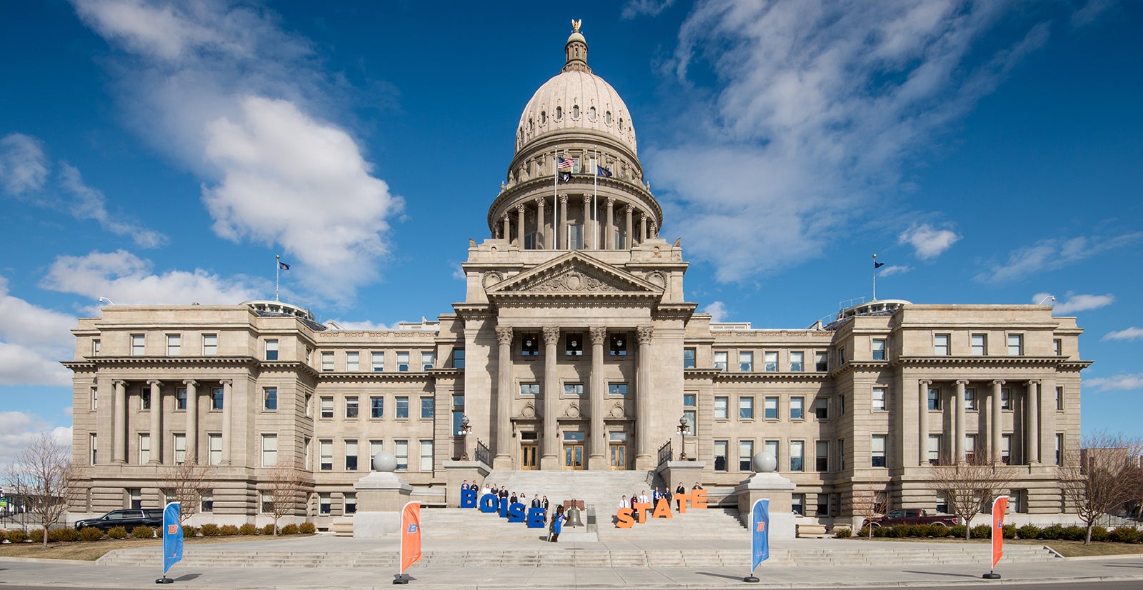 Students stand with Boise State flags and letters in front of Idaho state Capitol building