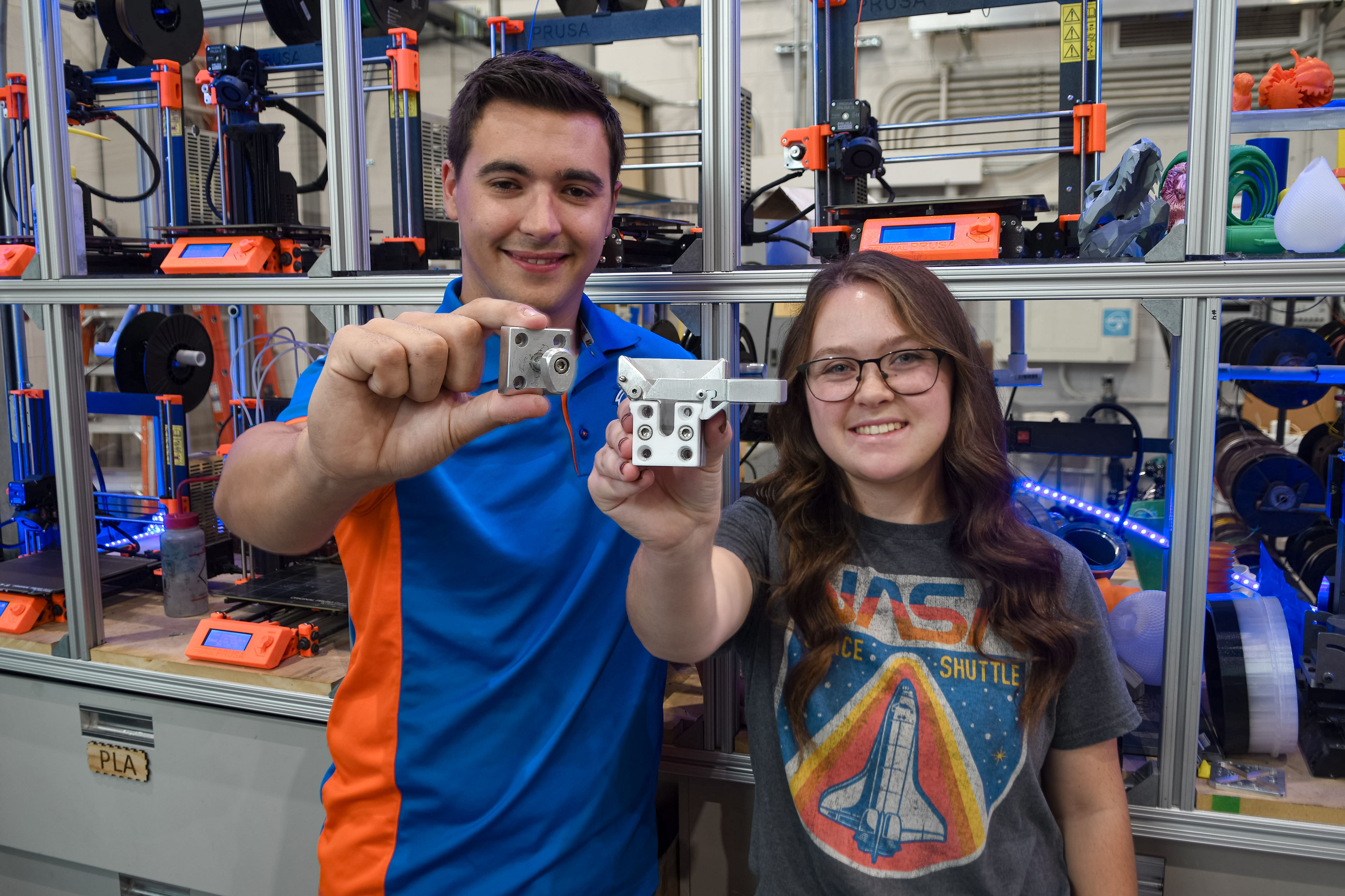 Two people in workshop holding 3D printed plastic pieces