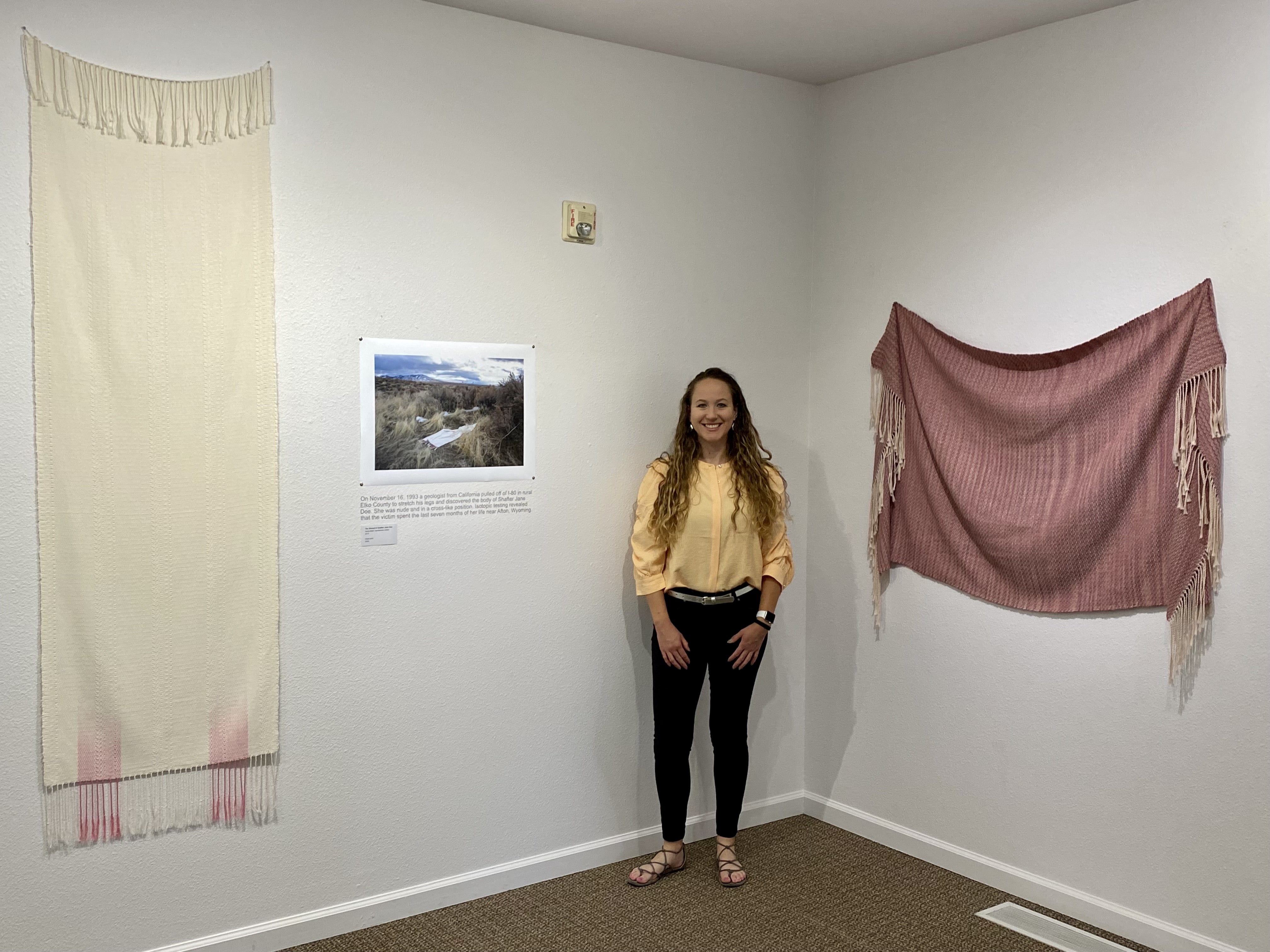 woman stands in museum exhibit surrounded by hanging woven shrouds