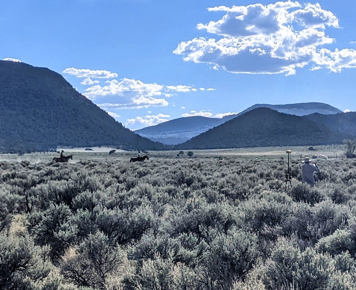 people riding horses across sagebrush steppe, mountains in distance