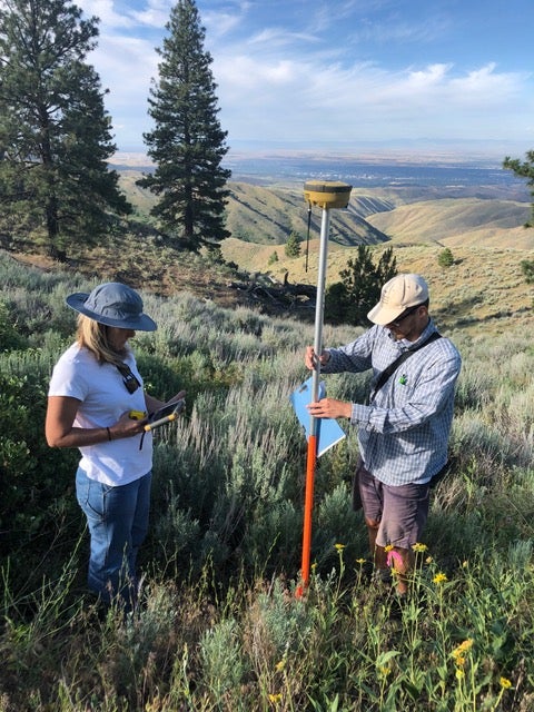 two people stand in sagebrush steppe with research equipment
