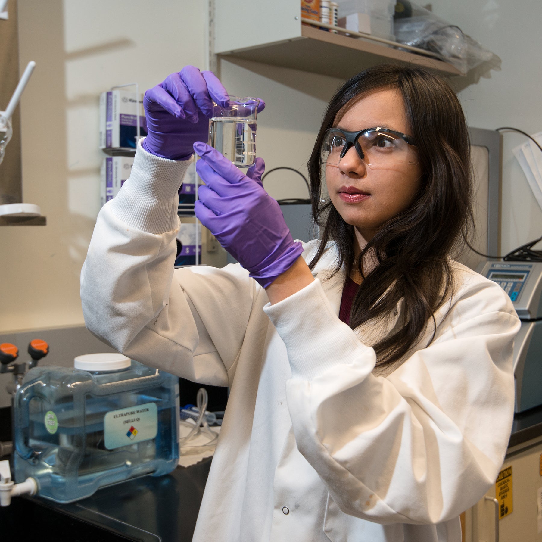 young woman in lab coat holds up beaker of clear liquid