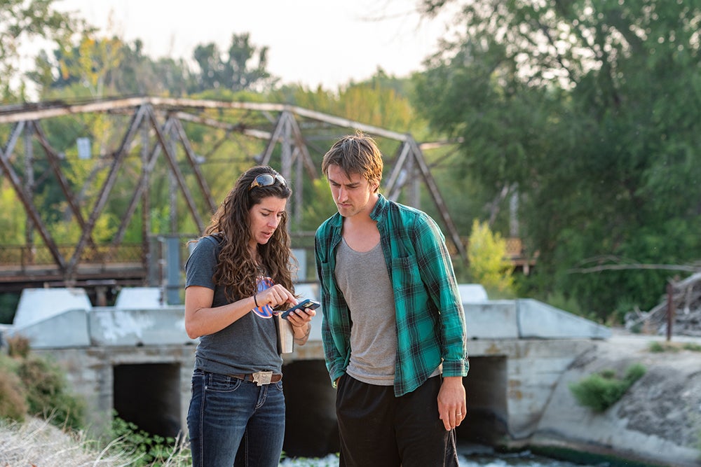 two people look at tablet while standing next to irrigation canal