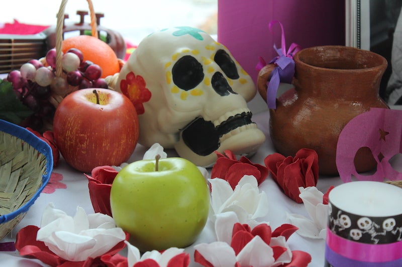Image of sugar skull on decorated table, with two apples and red and white flowers 