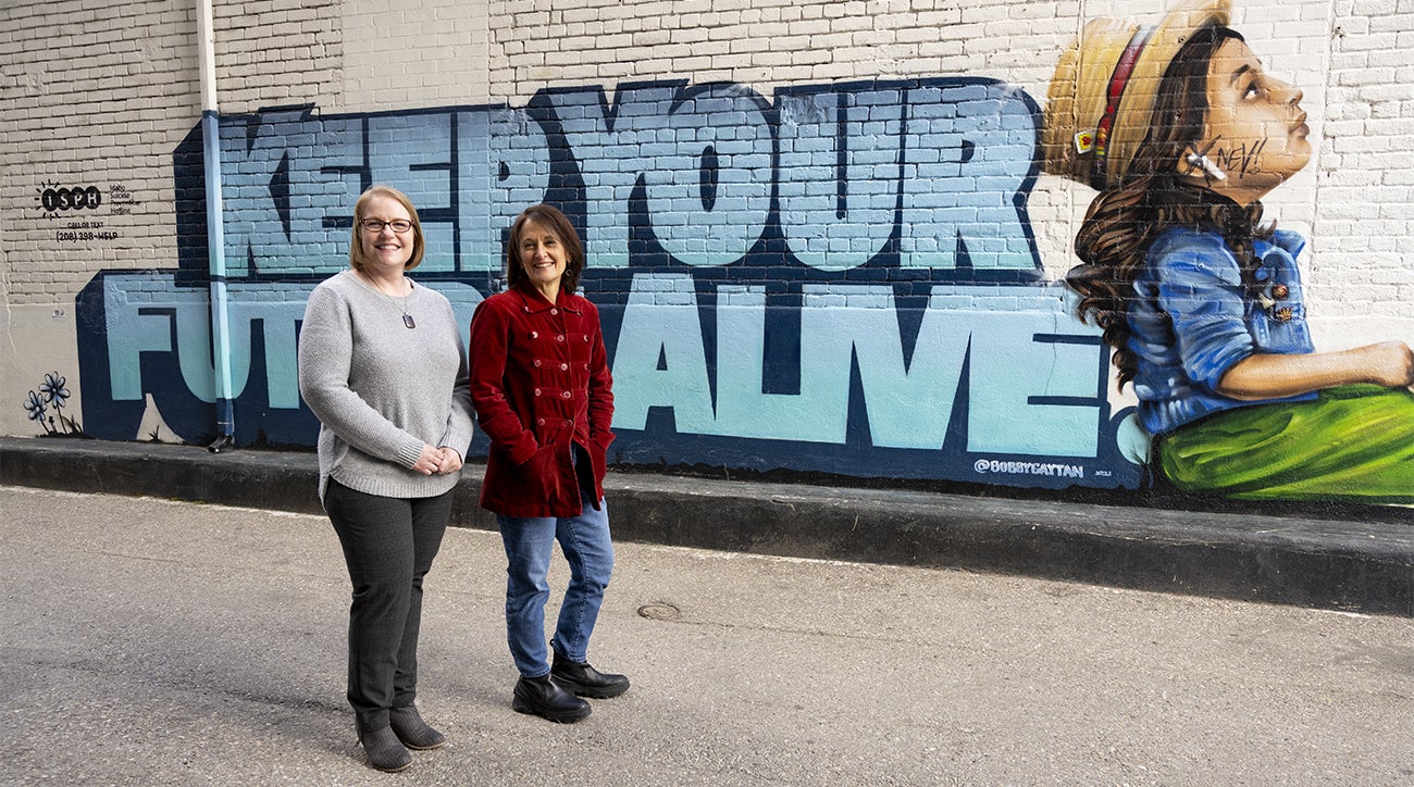 2 people standing in front of mural reading "Keep your future alive"