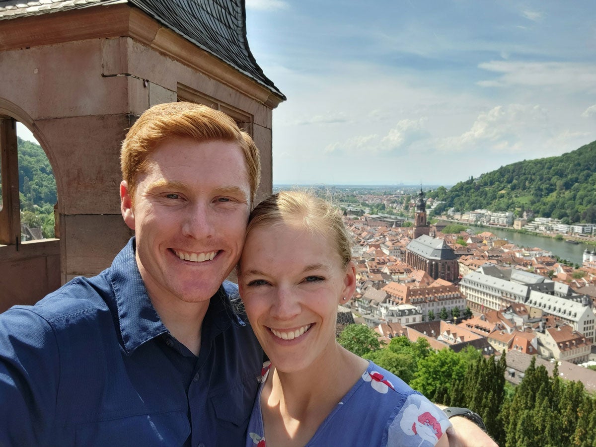 Joseph and Hannah smile with the skyline of a European city behind them.