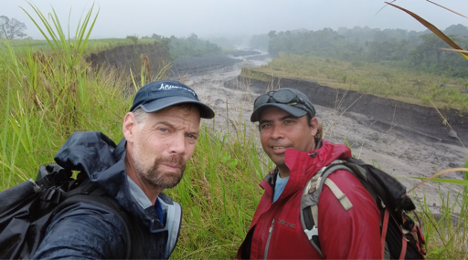  Two men stand beside large drainage pass filled with lahar