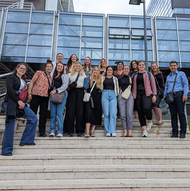 A group of students and professors stand on steps outdoors in front of a glass building in Croatia.