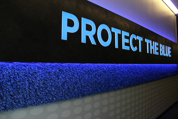 An illuminated sign says Protect the Blue and features blue colored synthetic turf below it
