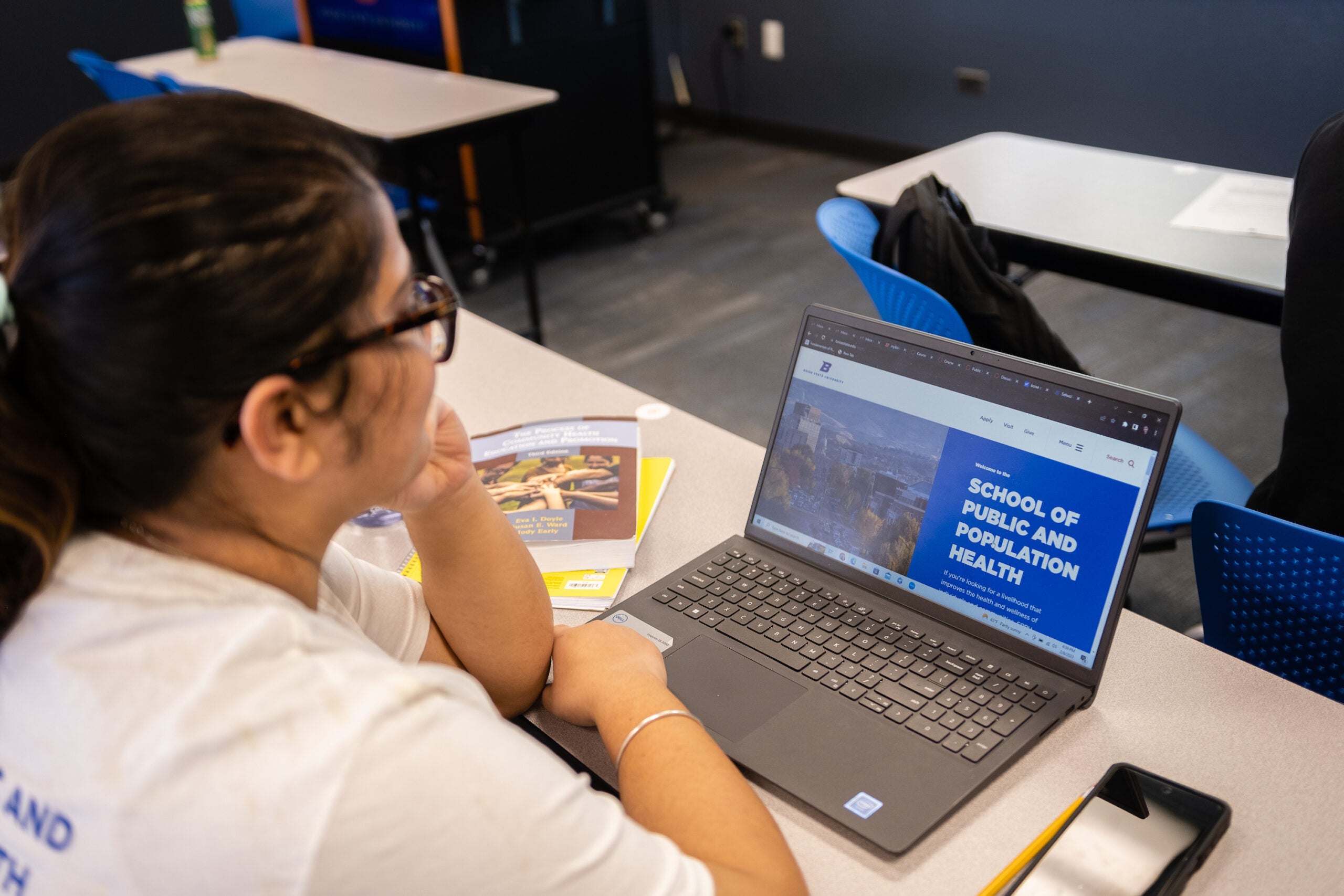 Student in classroom looks at a laptop with the School of Public and Population Health website on its screen.