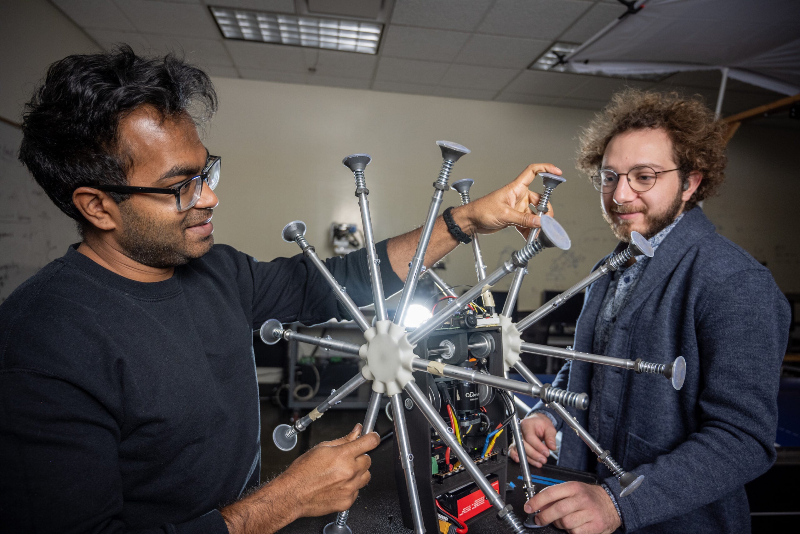 Two graduate students in the Mechanical and Biomedical Engineering program examine a robot in the Robot Control Lab.