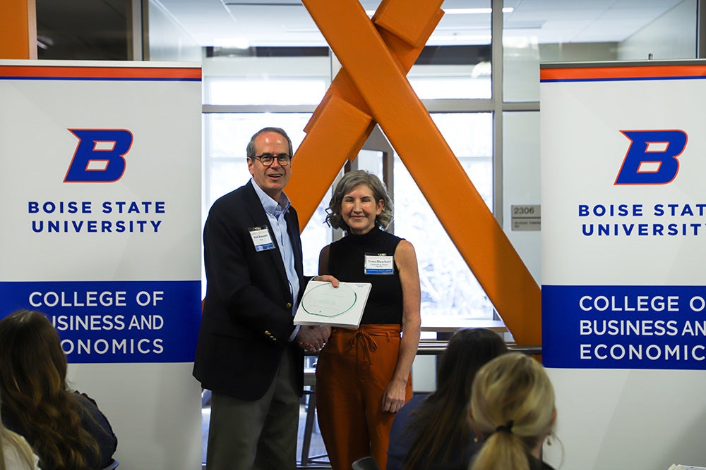 A dean shakes Trista Blanchard's hand and gives her a framed award. Banners on either side of them read Boise State University College of Business and Economics