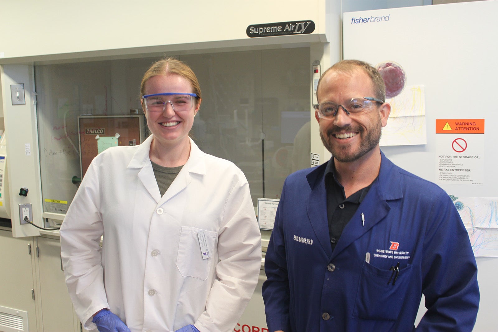 A chemistry professor and student posing for a photo in lab coats