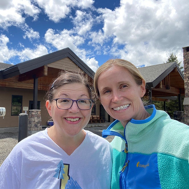 Llewellyn and Alderden stand and smile in front of a camp lodge building with blue skies overhead.
