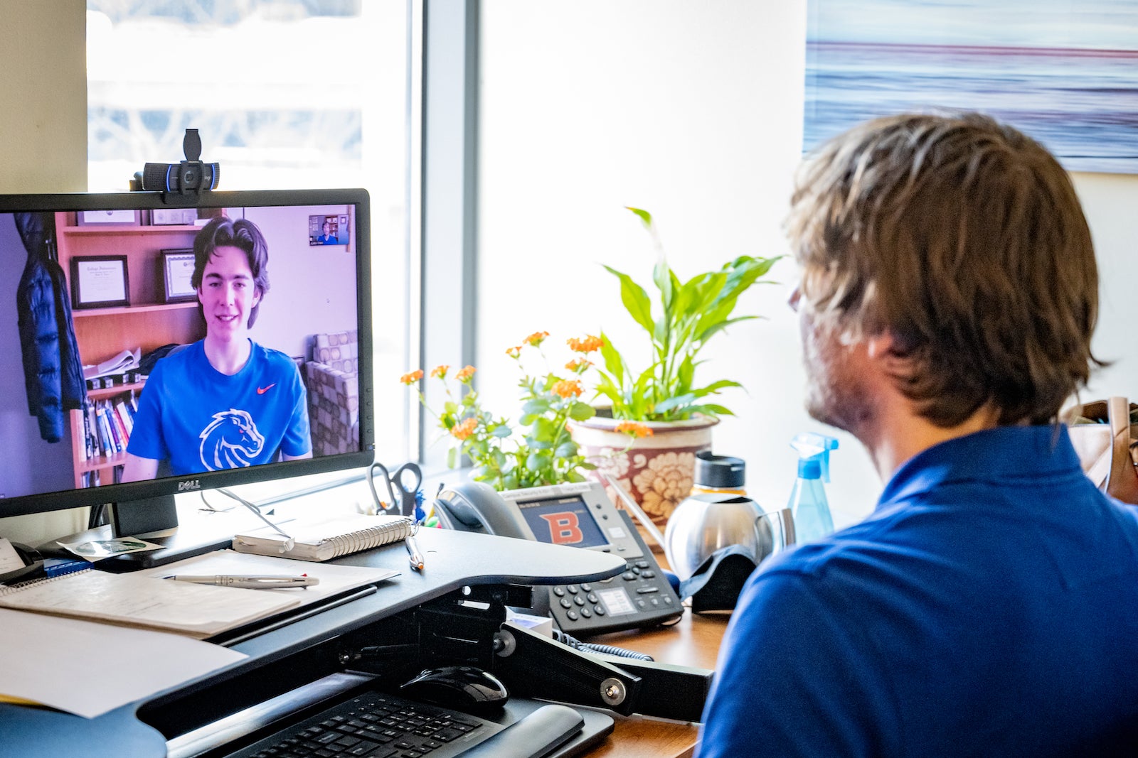 Student joining virtual meeting sitting in front of desk facing computer monitor