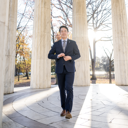 Ap person in a business suit stands outdoors in a circle of columns