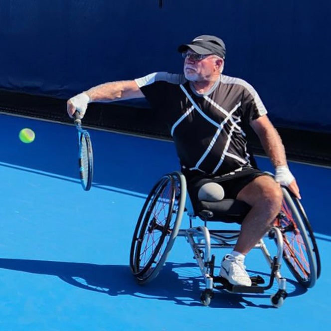 Kevin Falk lines his racket up to hit a tennis ball in his wheelchair during a game