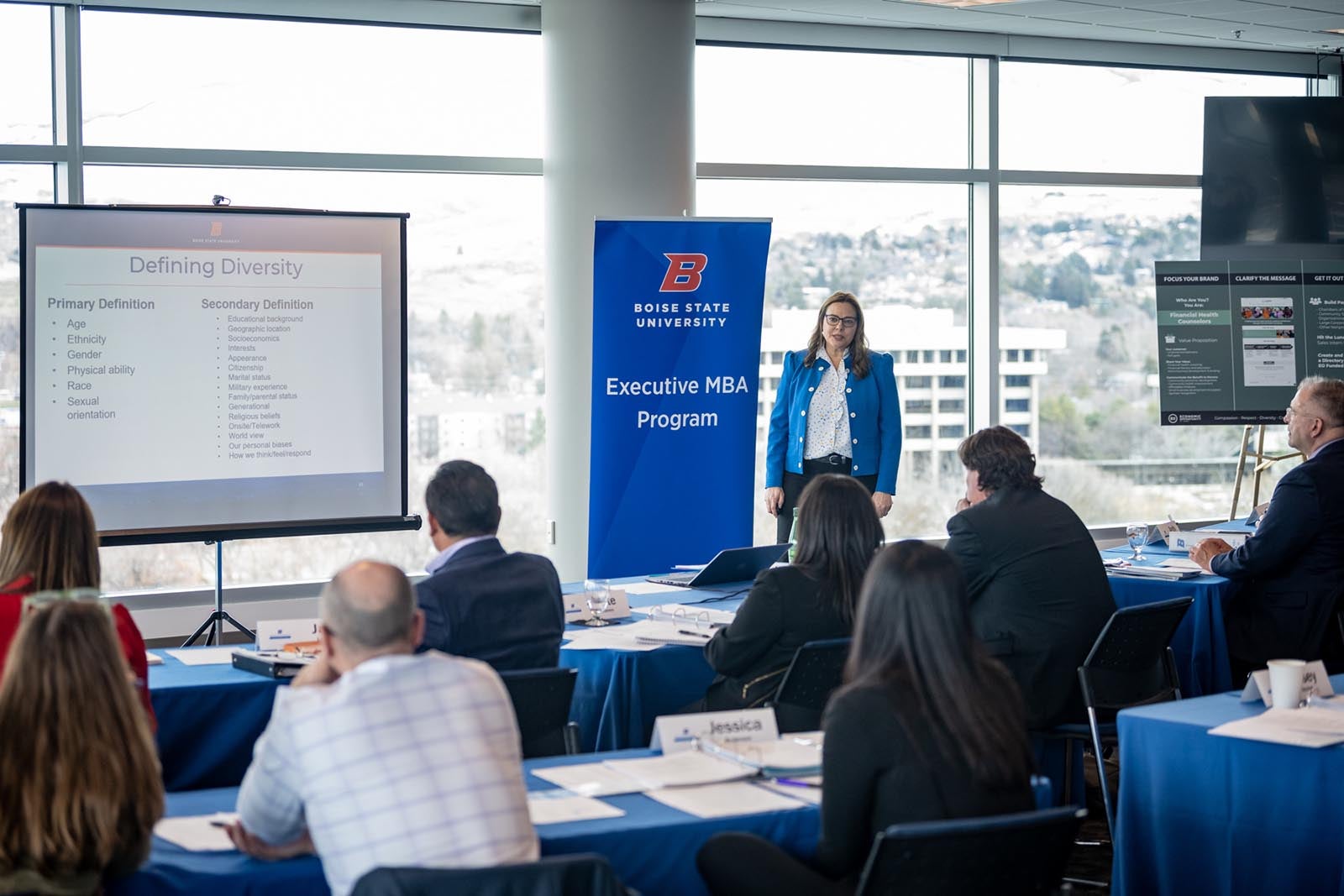 Instructor teaches a lesson from the front of a classroom full of students beside a Boise State Executive MBA banner.