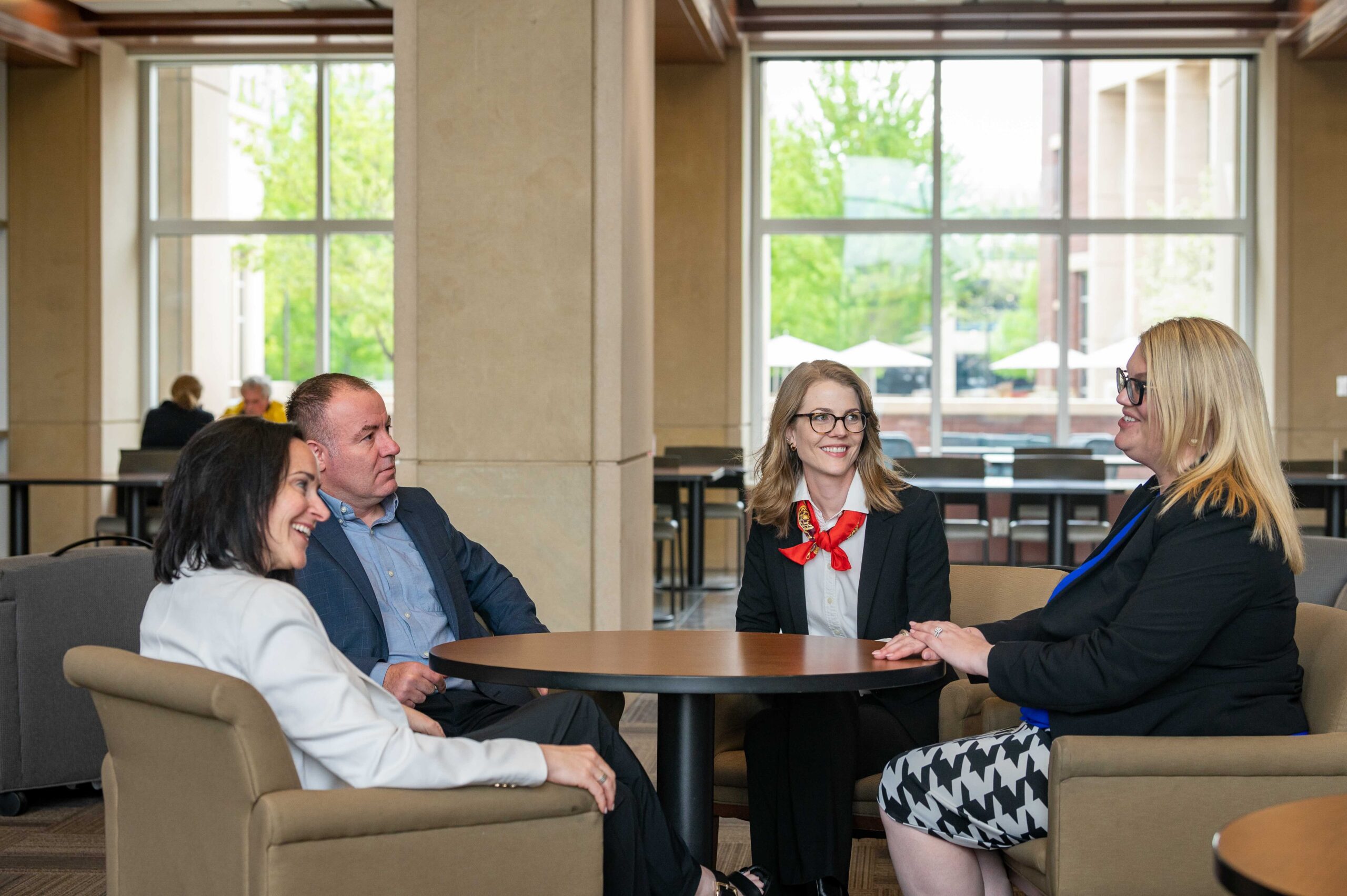 Four adults in business casual dress sit around a table socializing.