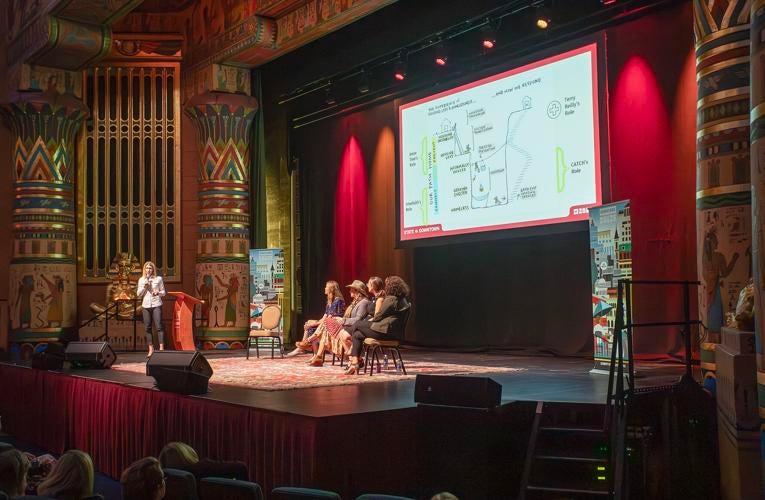 Persons sit on a panel on a stage