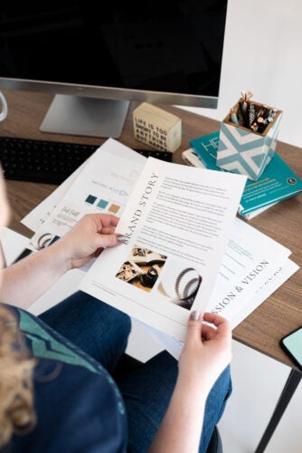 The camera looks over a woman's shoulder as she holds a document with pictures and text about branding. 