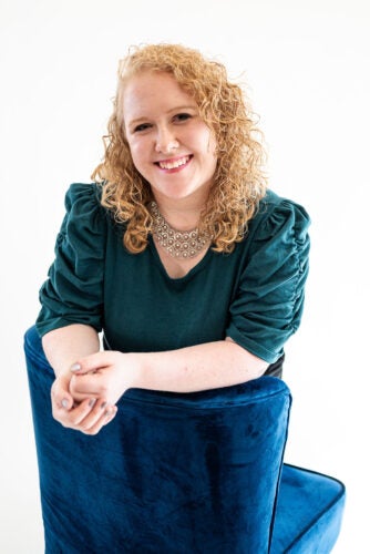 A woman with curly blonde hair wearing a dark green blouse smiles at the camera.