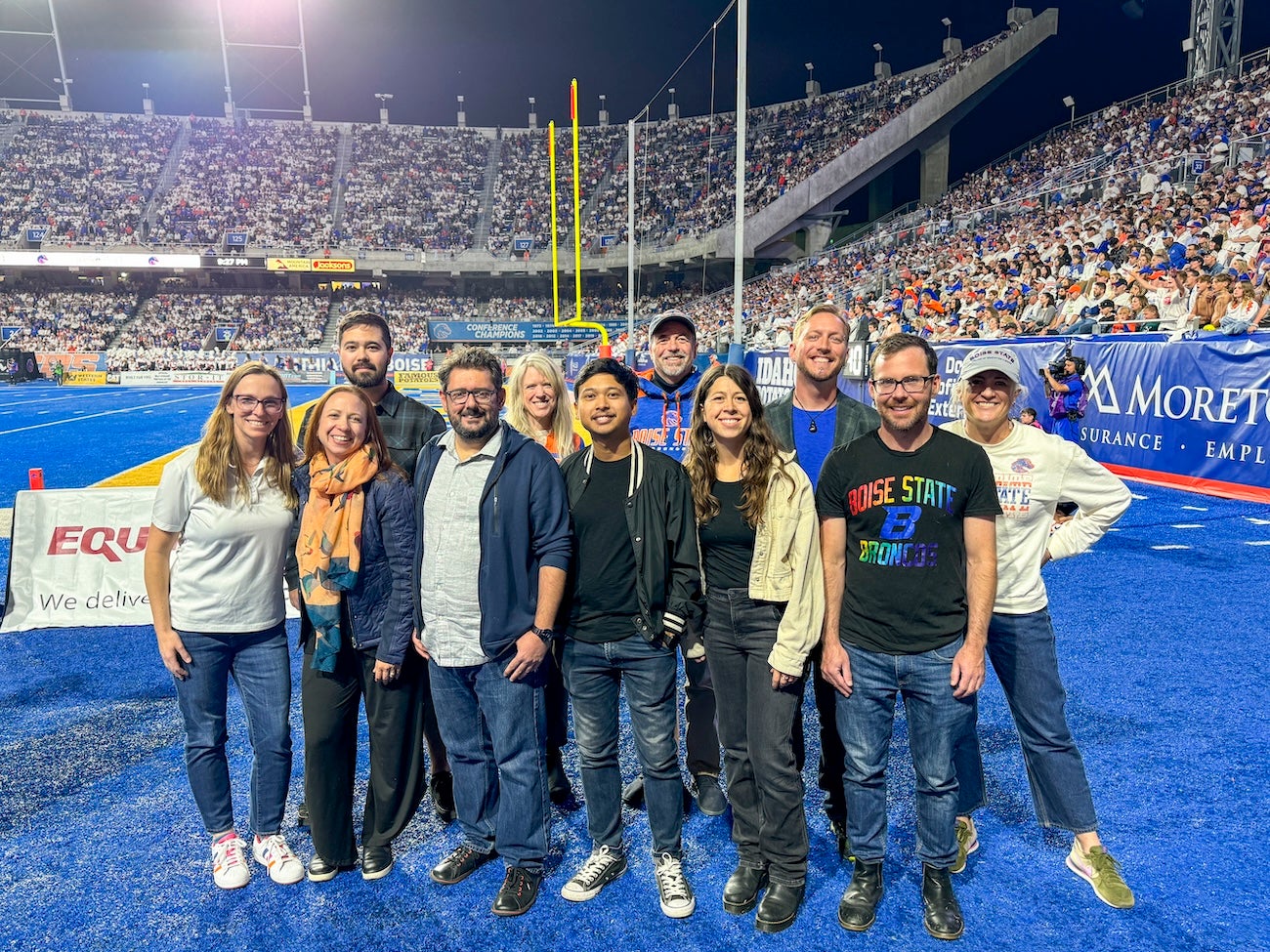 Persons pose on the blue field of Boise State