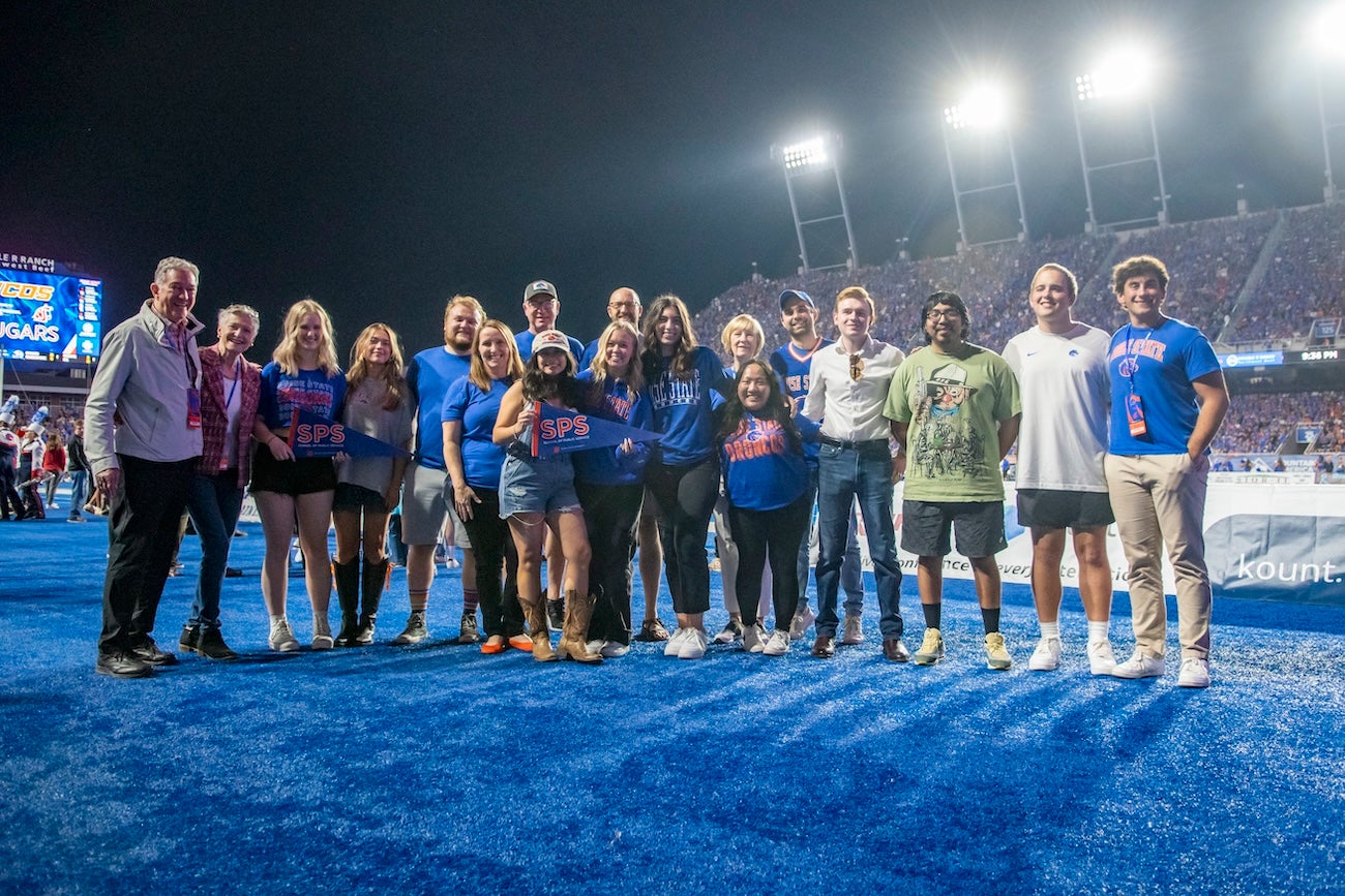 Persons pose on the blue field of Albertsons Stadium