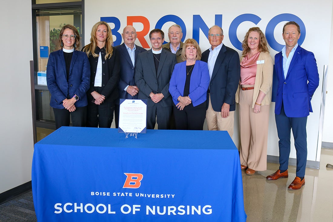 Nine people stand behind a table that has a formal scholarship agreement sitting framed on top.