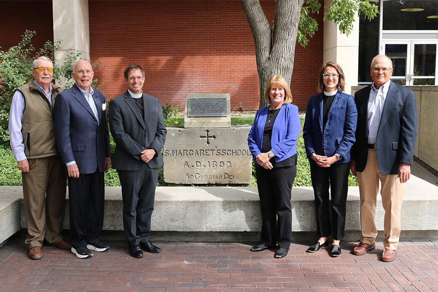 Six representatives from St. Michael's Episcopal Cathedral stand next to the original cornerstone from St. Margaret's school for girls.