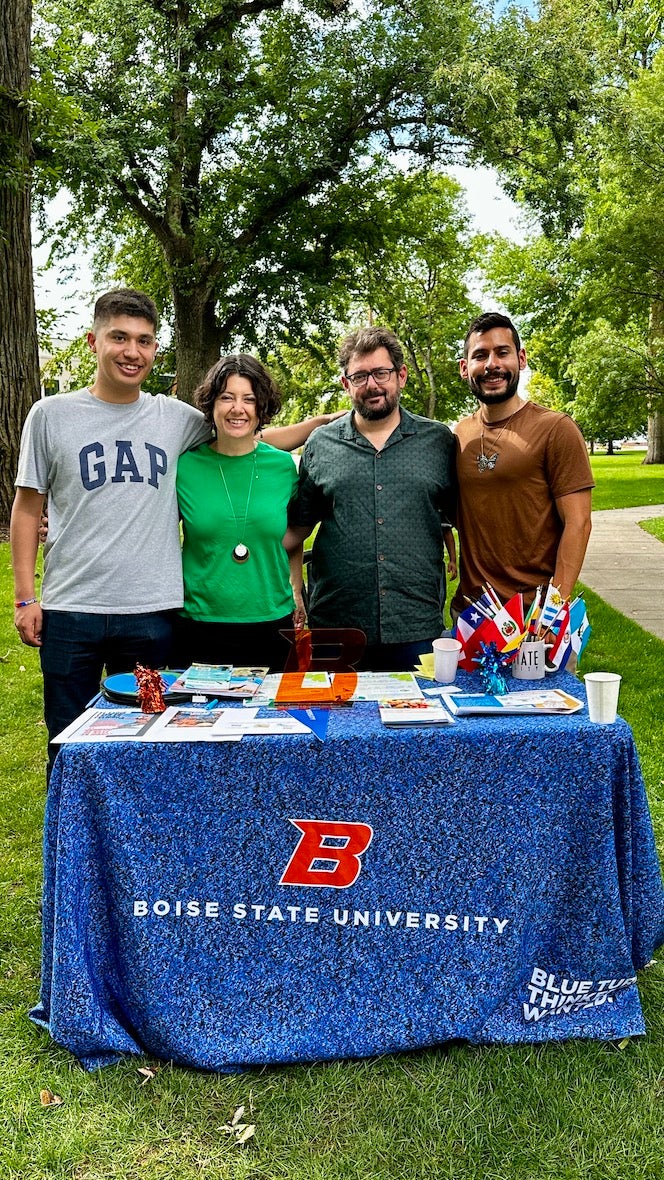 four people stand behind a table outside