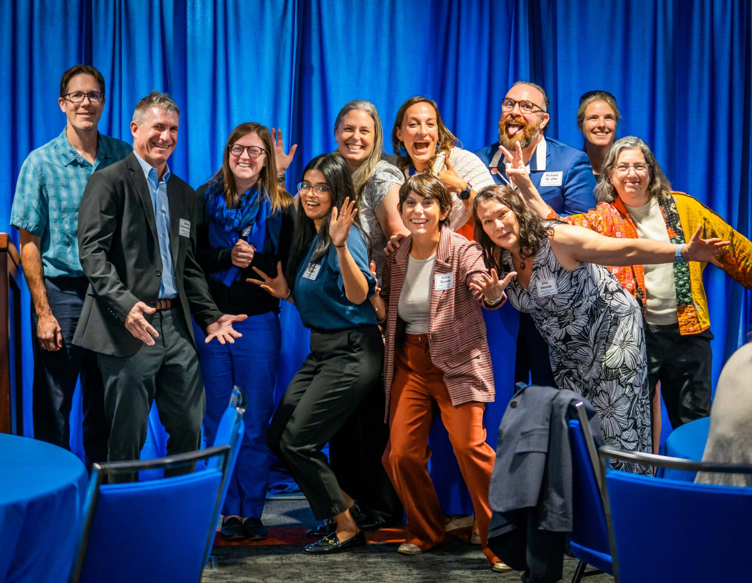 A group of persons pose in front of a blue fabric background